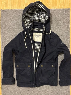 Vintage Abercrombie & Fitch Parkajacka - Säljer denna as feta Abercrombie & Fitch Fieldjackan med luva, med rutigt mönster inuti | Storlek S | Längd ≈ 66cm, Bredd armhåla - armhåla ≈ 52cm | Modell 175, 68kg | 