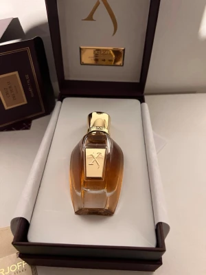 Xerjoff Oud Stars parfum i lyxig box - Exklusiv parfym från Xerjoff Oud Stars-serien. Flaskan är elegant med guldiga detaljer och genomskinligt glas som visar den bärnstensfärgade vätskan. Kommer i en lyxig mörklila och vit presentbox med gulddetaljer och logotyp. Perfekt för dig som gillar exklusiva dofter.
