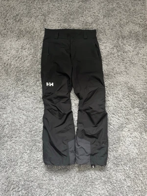 Svarta täckbyxor från Helly Hansen - Säljer ett par svarta täckbyxor från Helly Hansen i storlek S och säljs för 800kr!