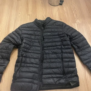 Svart dunjacka från Everest - Snygg svart dunjacka från Everest med quiltad design och dragkedja framtill. Jackan har två sidofickor med dragkedja och diskret logga på bröstet. Perfekt för kalla vinterdagar och riktigt lätt att bära. Osäker på storlek men tror M