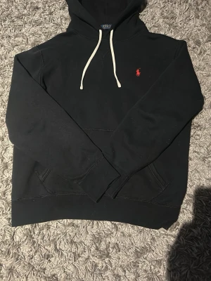 Svart hoodie från Polo Ralph Lauren, Knappt använd, säljer för den var för liten, Jag är 188 cm lång  - Svart hoodie från Polo Ralph Lauren med vit dragsko i huvan och röd broderad logga på bröstet. Klassisk känguruficka framtill och mjukt material som känns skönt mot huden. Perfekt för en avslappnad och stilren look. Kan diskutera priset.