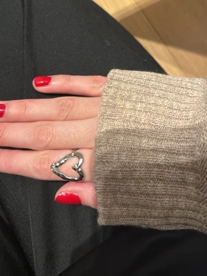 Silvrig hjärtformad ring - Trendig ring i silverfärgad metall med öppen hjärtformad design. Ringen har en modern och stilren look som passar perfekt för dig som gillar unika accessoarer. Enkel men ändå iögonfallande detalj till din outfit.