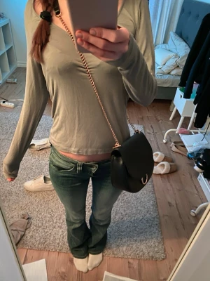 Svart axelväska med guldkedja - Jättefin svart axelväska i rundad form med guldfärgad kedjerem och dekorativ metallring på locket. Väskan är gjord i slätt konstläder och har en stilren, modern look som passar till många outfits💗