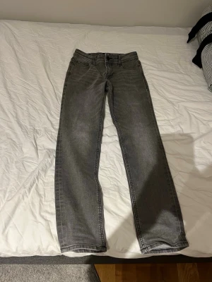 Grå raka jeans - Säljer ett par grå jeans med rak passform och klassisk femficksdesign. Jeansen har normal midja och är tillverkade i ett mjukt denimtyg. Perfekta för en avslappnad och stilren look.