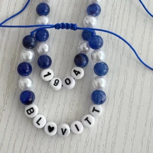 Blåvitt pärlarmband med text💙🤍 - Handgjort armband med blå och vita pärlor på blått snöre. Armbandet har vita bokstavspärlor med texten 'BL💙VITT' och '1904'. Perfekt accessoar för dig som gillar personliga smycken och vill visa ditt stöd för Blåvitt.