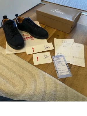 Mörkblåa mocka sneakers från Christian Louboutin - Snygga svarta sneakers från Christian Louboutin i mocka med klassisk låg siluett och svarta skosnören. Insidan är fodrad i beige läder.!!!! De ända defekta är sko snörena som har tappat plast biten som sitter längst ut. Kvittot påsen o de grejerna på första bilden följer ej med!!!!!