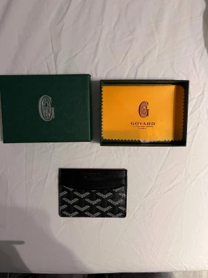 G-plånbok - Snygg och stilren i färgen svart med deras ikoniska mönster. Plånboken har flera kortfack och är tillverkad i skinn med tryckt logga framtill. Perfekt för dig som vill ha något exklusivt och smidigt i fickan.  