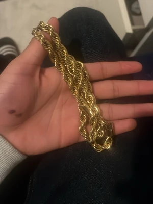 Tjockt guldfärgat kedjehalsband - Säljer ett chunky halsband i guldfärgad metall med tvinnad kedjedesign. Halsbandet har en rejäl och iögonfallande look som passar perfekt för dig som vill sticka ut. Låset är robust och smycket känns riktigt trendigt.
