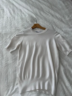 Vit kortärmad topp från Zara - Säljer en stilren vit topp från Zara med rund halsringning och korta ärmar. Toppen har en enkel, clean design och är gjord i ett mjukt, tunt material som känns skönt mot huden. Perfekt att matcha med jeans eller kjol för en fräsch look.