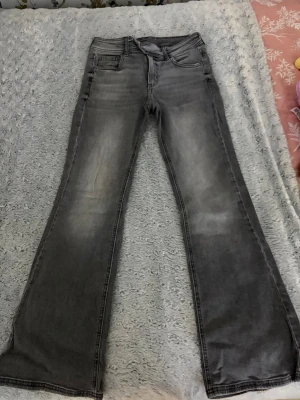 Grå bootcut jeans  - Säljer ett par grå bootcut jeans med snygga slitningar och tvättade detaljer. Jeansen har fem fickor, dubbla knappar i midjan och klassisk dragkedja. Perfekta för dig som gillar en avslappnad men trendig look.