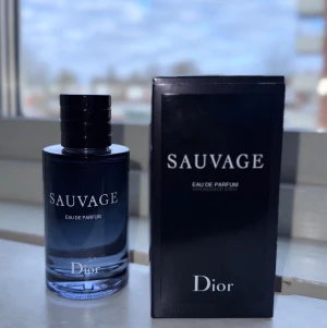 Dior Sauvage Eau de Parfum 100ml (INTE ORIGINAL) - Dior Sauvage Eau de Parfum är en ikonisk herrdoft i en elegant mörkblå glasflaska med svart lock. Flaskan rymmer 100 ml och kommer i en stilren svart kartong med vit text. Doften är modern och maskulin, perfekt för dig som vill sticka ut.