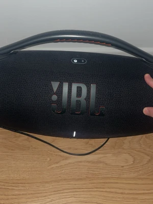 JBL Boombox 3 bärbar högtalare svart - Stor och kraftfull JBL Boombox 3 bärbar högtalare i svart med robust handtag och mesh-tyg. Utrustad med USB-port, AUX-ingång och laddningskontakt. Perfekt för att ta med sig musiken överallt tack vare det tåliga materialet och den ikoniska designen. Använd litegrann och små skrapor som är synliga i bilderna. Pris kan disktuteras !!