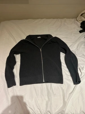 Svart ribbad ziptröja - Säljer en svart ribbad ziptröja med huva från märket C. Tröjan har dragkedja framtill, långa ärmar och breda muddar vid ärmslut och nederkant. Perfekt för en avslappnad och stilren look.