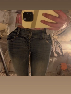 Blå bootcut jeans med slitningar - Säljer ett par blå bootcut jeans med  lätt tvättade detaljer på låren. Jeansen har låg midja, dubbla knappar och klassiska fem fickor. 🩷 