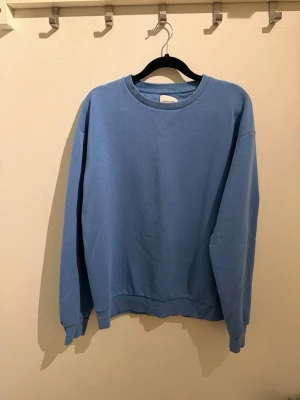 Blå crewneck sweatshirt - En enkel och stilren blå crewneck sweatshirt från Weekday. Tröjan har rund halsringning, långa ärmar och ribbade muddar vid ärmslut och nederkant. Tillverkad i mjukt bomullsmaterial som känns skönt mot huden. Perfekt för en avslappnad och trendig look.