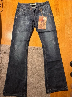 Mörkblå bootcut jeans från K.E.J. - Säljer ett par mörkblå bootcut jeans från K.E.J. Jeansen har slitna detaljer, fem fickor och klassiska kopparfärgade nitar. Materialet är denim i bomull och passformen är utsvängd nedtill. Perfekta för en avslappnad och trendig look.