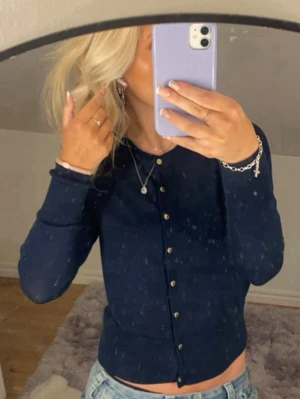 Mörkblå ribbad kofta med knappar - Trendig mörkblå ribbad kofta med guldfärgade knappar framtill. Koftan har rund halsringning och långa ärmar, perfekt att styla med jeans eller kjol för en snygg look.