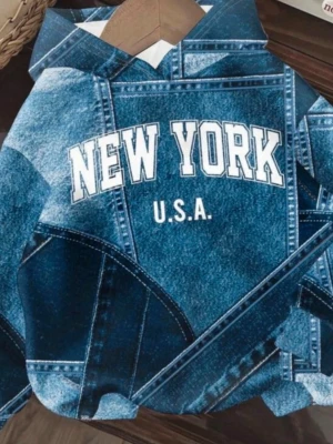 Blå hoodie med New York-tryck - Snygg hoodie med blått denim-mönster och texten 'NEW YORK U.S.A.' i vitt framtill. Hoodien har huva och en avslappnad passform. Perfekt för dig som gillar streetwear och vill sticka ut med ett coolt tryck. Materialet ser ut som bomull eller polyester.