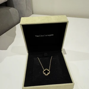 Klöver halsband svart - Supersnyggt nytt halsband som använts en gång och är i princip helt nytt. Kedjan är tunn och elegant, och hänget är tillverkat i äkta silver men doppat i guld därav den gulda färgen! Lådan medföljer dock inte 