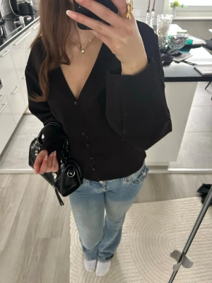 Svart v-ringad blus med knappar - Stilren svart blus med djup v-ringning och knäppning framtill. Blusen har långa ärmar och en rak passform💕