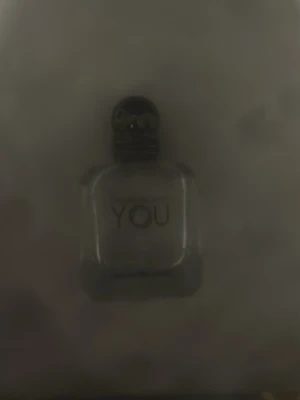 Tom Emporio Armani Stronger With You parfym - Emporio Armani Stronger With You är en elegant parfym i en genomskinlig glasflaska med rundade kanter och svart kork. Flaskan har en stilren och modern design med märkets logga och doftnamnet tryckt på framsidan.