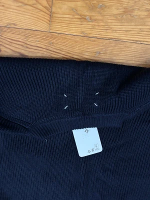 Mörkblå stickad tröja Maison Margiela - Snygg mörkblå stickad tröja från Maison Margiela i grov ribbstickning. Tröjan har rund halsringning och klassisk passform. Perfekt för dig som gillar stilrena och exklusiva plagg.