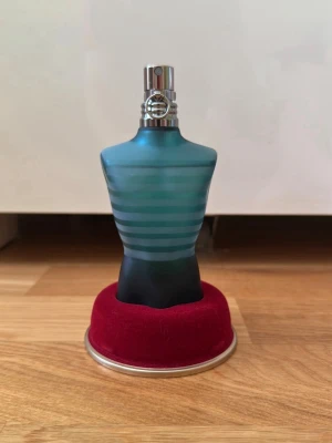 Jean Paul Gaultier Le Male parfym - Ikonisk parfymflaska formad som en manlig torso i blått och svart glas med turkosa ränder. Kommer med original metallburk och röd sammetsbas. En klassiker från Jean Paul Gaultier som sticker ut i badrumshyllan. Helt oanvänd. Köpt hos lyko. 
