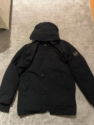 Svart Canada goose Dunn jacka  - Säljer denna Canada goose Dunn jackan pga använder den ej längre. Skick 8/10. Jackan är i jätte bra skick. Jackan har även knappar på framsidan. Perfekt för den kalla vintern!! Vid diskussion om pris skriv! Rep!