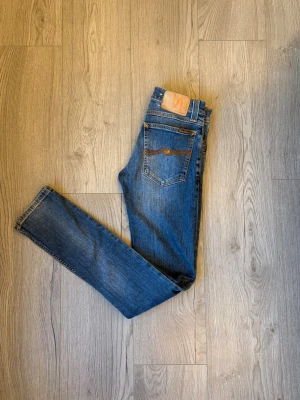 Blå jeans från Nudie Jeans - Säljer ett par klassiska blå  jeans från Nudie Jeans. Jeansen har en smal passform och är gjorda i denim. Perfekta för dig som gillar en tidlös och avslappnad stil. Modelln är tight long john. Priset inte hugget i sten 🪨 🔨