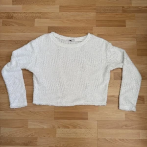 Vit cropped stickad tröja - Säljer en vit cropped stickad tröja med lång ärm och rund hals. Tröjan har en fluffig struktur och är perfekt för att skapa en chill och trendig look. Passar till både jeans och kjol för en avslappnad stil.