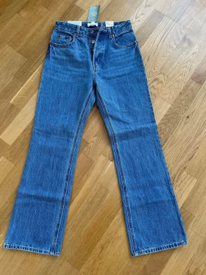 Blå raka jeans från H&M - Säljer ett par klassiska blå jeans från H&M med rak passform och hög midja. Jeansen är tillverkade av denim med 20% återvunnen bomull och har fem fickor samt knappgylf. Perfekta för en avslappnad och trendig look.