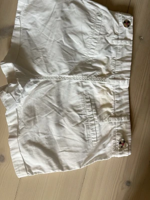 Vita bomullsshorts med knappar - Snygga vita shorts i bomull. Shortsens midja är normal och de har fickor både fram och bak. Perfekta för varma dagar och en stilren look. De är svala och luftiga så passar bra till sommaren.