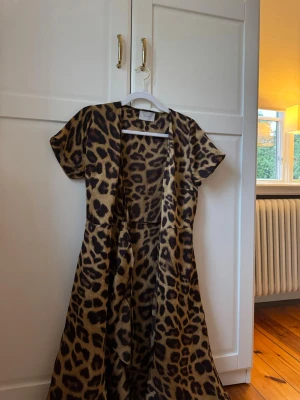 Leopardmönstrad långklänning - Cool omlott långklänning med leopardmönster och korta ärmar. Klänningen har en figurnära passform upptill och faller snyggt nedåt. Perfekt för dig som vill sticka ut med ett djurmönster. Materialet känns mjukt och följsamt.
