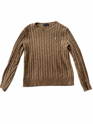 Beige kabelstickad tröja från Polo Ralph Lauren - Kabelstickad tröja i beige från Polo Ralph Lauren med rund halsringning och långa ärmar. Tröjan har ribbstickade muddar vid ärmslut och nederkant samt en liten broderad logga på bröstet. Perfekt för lager-på-lager-stil.