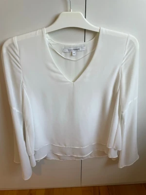 Vit v-ringad blus från Banana Republic - Stilren vit blus från Banana Republic med v-ringning och långa, lätt utsvängda ärmar. Tillverkad i ett tunt, mjukt tyg som faller snyggt. Perfekt att matcha med både jeans och kjol för en trendig look.