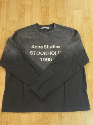 Svart långärmad topp Acne Studios - Cool svart långärmad topp från Acne Studios med tryck i vitt framtill där det står 'Acne Studios STOCKHOLM 1996'. Rund halsringning och relaxed fit. Perfekt för dig som gillar streetwear och enkel stil.