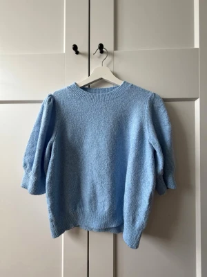 Ljusblå stickad tröja Vero Moda - Mysig ljusblå stickad tröja från Vero Moda med puffärmar och ribbade muddar vid hals, ärmslut och nederkant. Tröjan har en avslappnad passform och är perfekt för lager på lager. Materialet känns mjukt och behagligt mot huden.