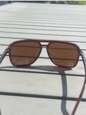 Solglasögon  - Snygga solglasögon i klassisk aviator-modell med bruna bågar och bruna tonade glas. Ramen har en retrovibe och är tillverkad i plast. Perfekta för dig som vill ha en cool och tidlös look i solen.