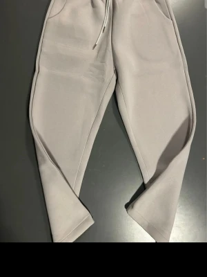 Beige mjukisbyxor med broderad ficka - Säljer ett par beige mjukisbyxor med dragsko i midjan och två sidofickor fram. På baksidan finns en ficka med broderat 'A*'. Byxorna har raka ben och är gjorda i mjukt, bekvämt material som passar perfekt för chill dagar.