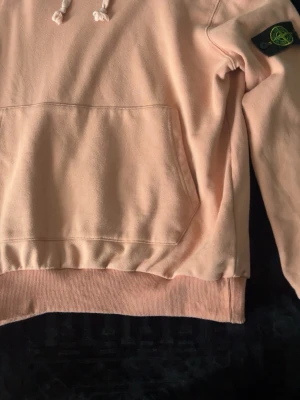 Ljusrosa hoodie från Stone Island - Säljer en ljusrosa hoodie från Stone Island med klassisk patch på ärmen. Hoodien har huva med dragsko, magficka och ribbade muddar. Tillverkad i mjuk bomull för skön känsla och avslappnad stil, tröjan har krympt med tiden så den är i storlek S-M idag. 