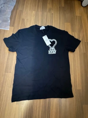 Ami Paris - T-shirt - Snygg svart t-shirt från Ami med stor vit hjärtformad logga på bröstet. Klassisk rund hals och korta ärmar. Tillverkad i mjuk bomull för skön känsla och stilren look.
