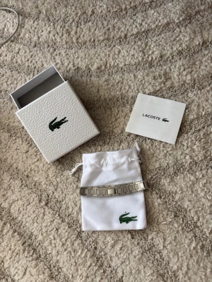 Silverfärgat armband från Lacoste - Snyggt armband i silverfärgad metall från Lacoste med länkdesign och diskret Lacoste-logga på mitten. Kommer med original ask och tygpåse med krokodil-logga. Perfekt accessoar för dig som gillar stilrena detaljer.