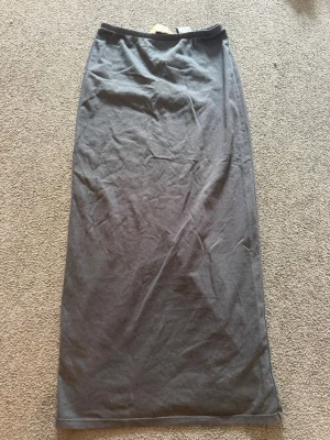 Grå långkjol med slits - En stilren grå långkjol med rak passform och slits baktill. Kjolen har resår i midjan och är tillverkad i ett mjukt, stretchigt material som känns bekvämt hela dagen. Perfekt att matcha med en crop top eller oversized tröja.
