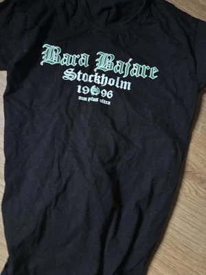 Svart Bara Bajare t-shirt Stockholm - Säljer en svart t-shirt från Bara Bajare med tryck i vitt och grönt på bröstet där det står 'Bara Bajare Stockholm 1996 non plus ultra'. Klassisk passform och rund hals. Perfekt för dig som vill visa ditt stöd för Bajen.