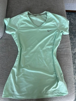 Mintgrön Nike Pro träningströja - Snygg mintgrön träningströja från Nike Pro med V-ringning och korta ärmar. Storlek L men passar M också men den är lång i modellen 