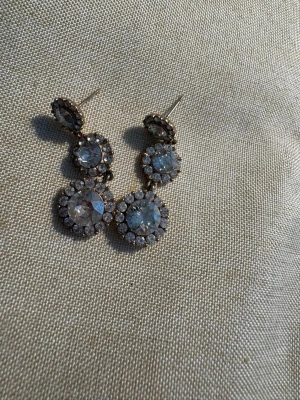 Lily and Rose örhängen  - Säljer ett par eleganta örhängen i guldton med tre runda hängen på varje, dekorerade med gnistrande klara stenar i mitten och små stenar runtom. Perfekta för dig som gillar att sticka ut med accessoarer som fångar ljuset.