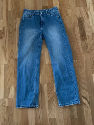 Blå raka jeans från Dr. Denim - Säljer ett par klassiska blå jeans från Dr. Denim med rak passform och fem fickor. Jeansen har en ljus tvätt och är tillverkade i bomull. Perfekta för en avslappnad och trendig look.
