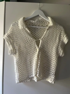Vit virkad kortärmad topp - Säljer en vit, virkad cardigan med korta ärmar och krage. Tröjan har knappar framtill och ett luftigt, nätliknande mönster. 