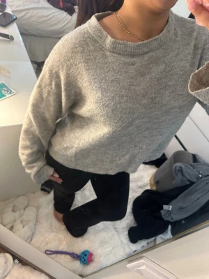 Grå croppad stickad tröja - Mysig grå stickad tröja med croppad passform och rund hals. Perfekt till både jeans och leggings för en chill look. Tröjan har långa ärmar och är enkel att matcha med olika stilar.den har fläckar här och där
