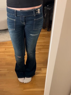 Low waist jeans med hål - Säljer dessa mörkblå bootcut jeans med slitningar och två knappar i midjan. Använda ca 3 gånger 🥰